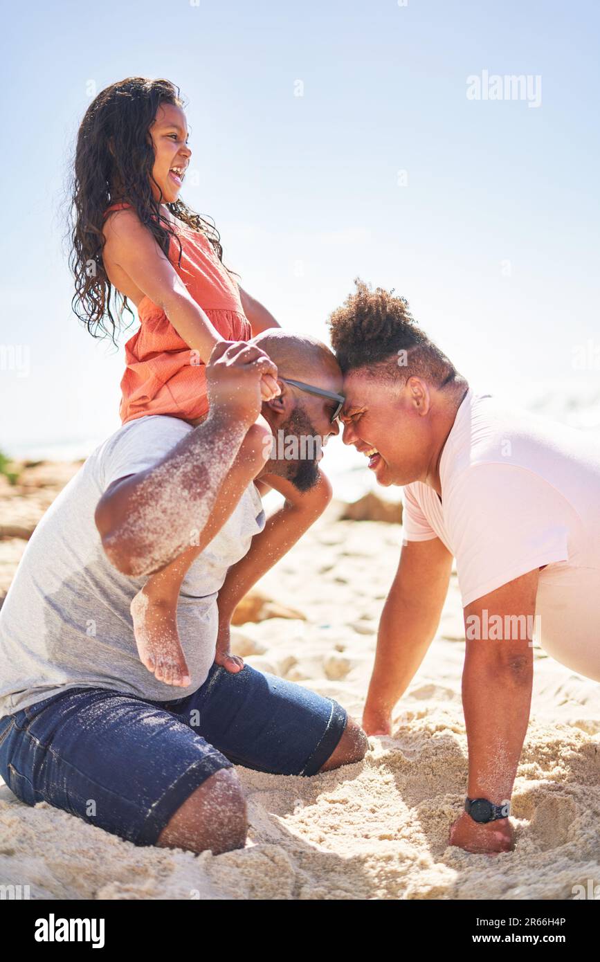 Happy, affectionate gay male couple with daughter on sunny beach Stock Photo