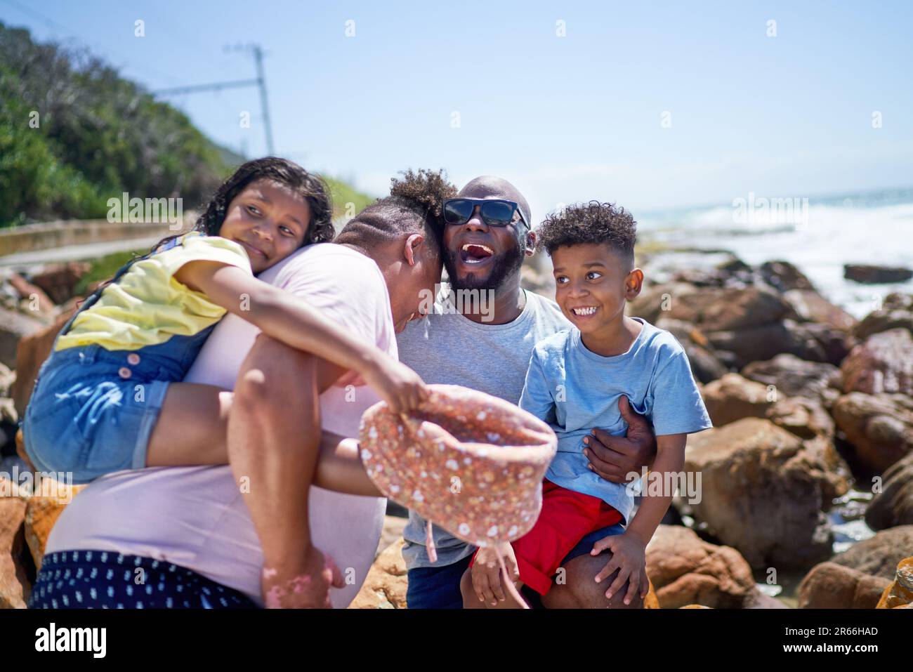 Happy gay male couple and kids laughing on sunny beach rocks Stock Photo