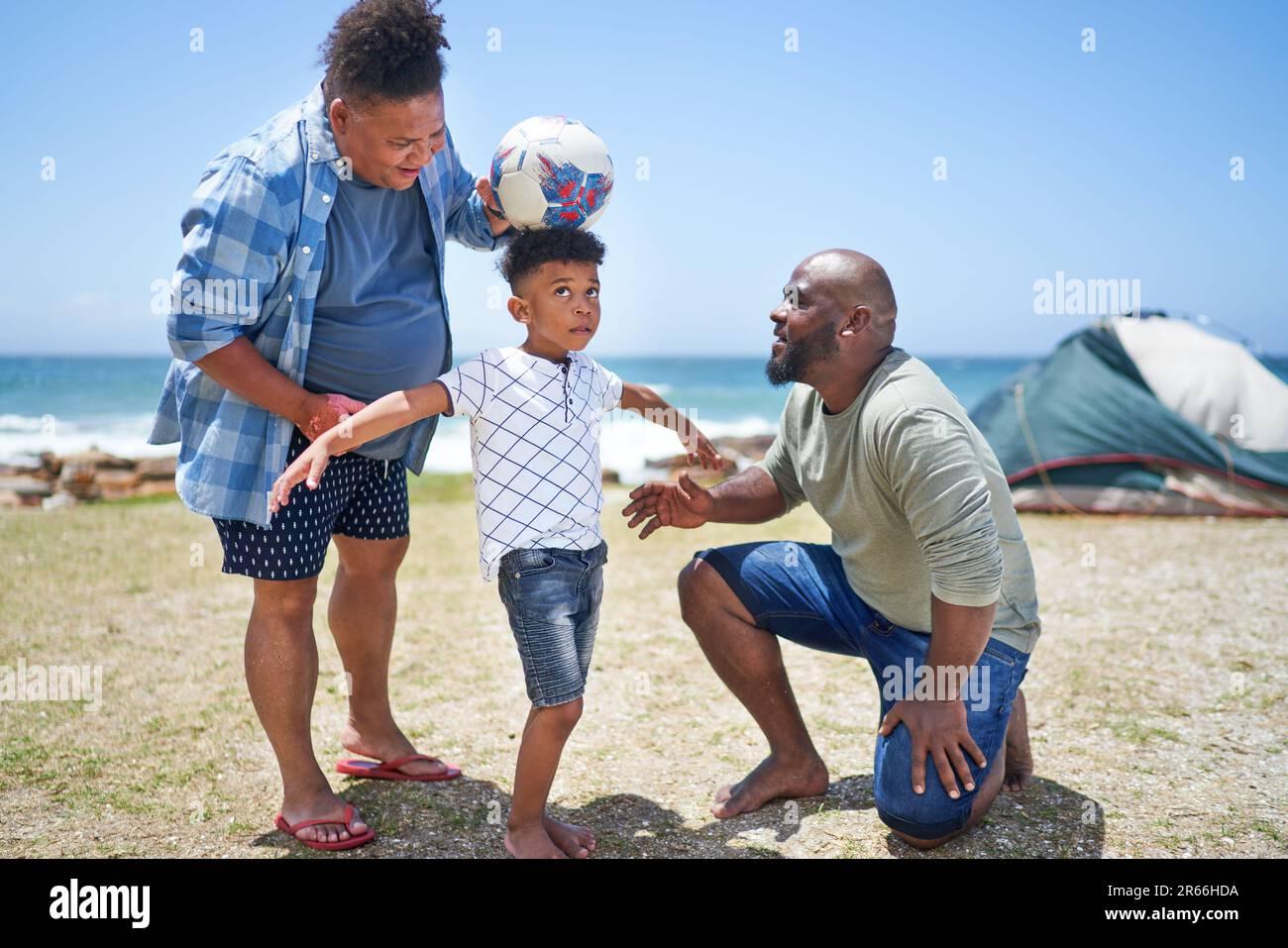 Gay male couple and son playing with soccer ball on sunny beach Stock Photo