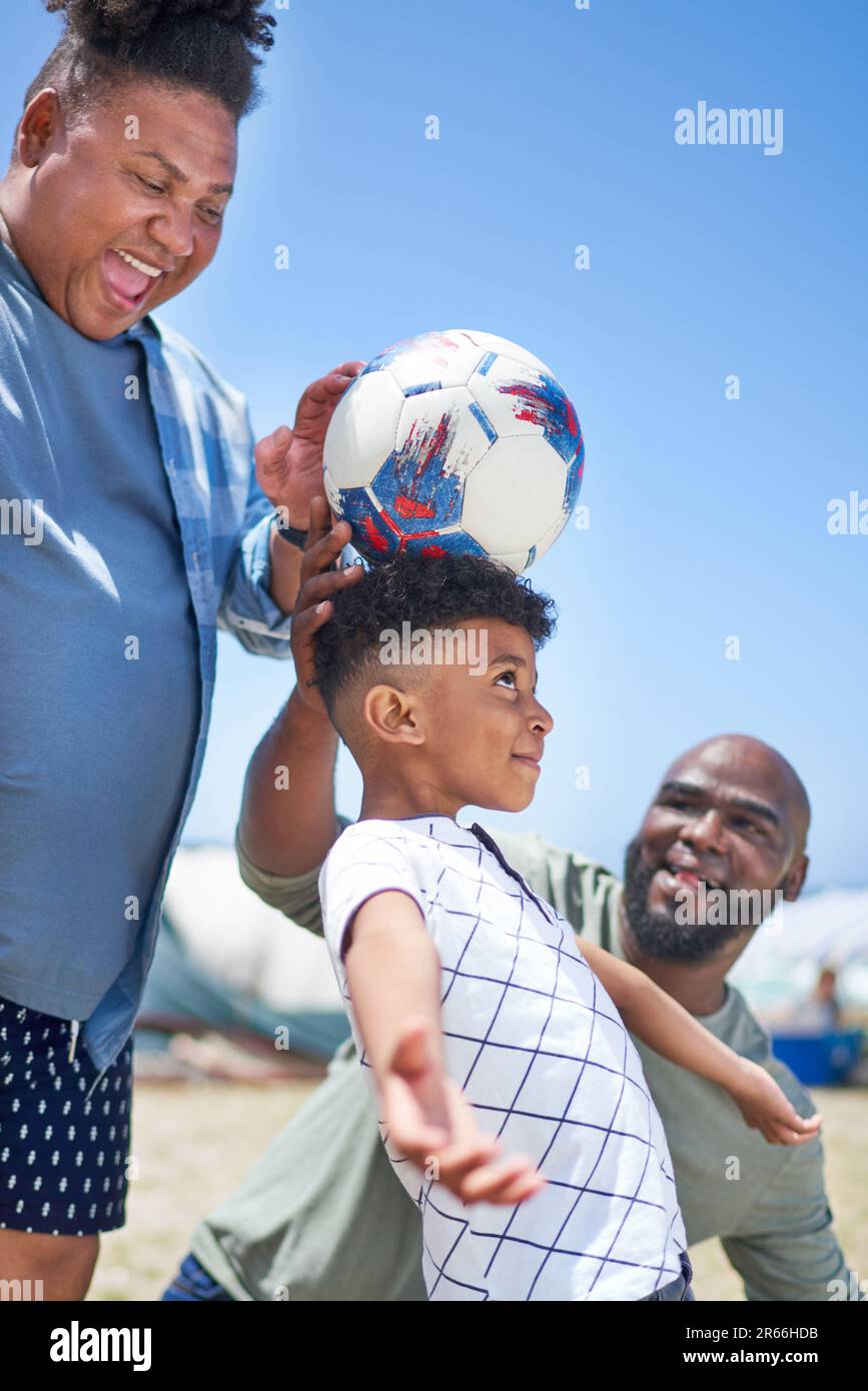 Happy gay male couple and son playing with soccer ball on sunny beach Stock Photo