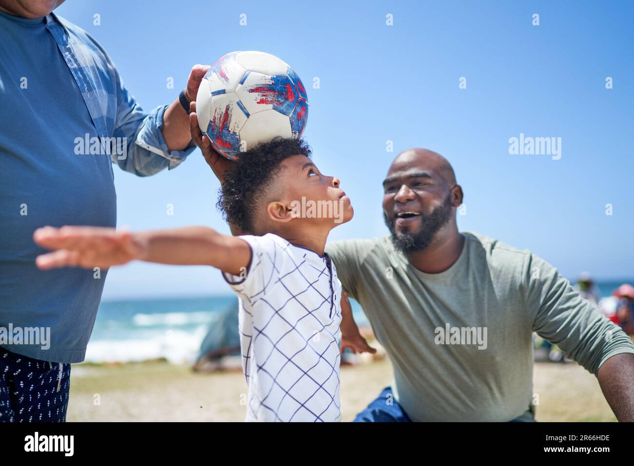 Gay male couple and son playing with soccer ball on sunny beach Stock Photo