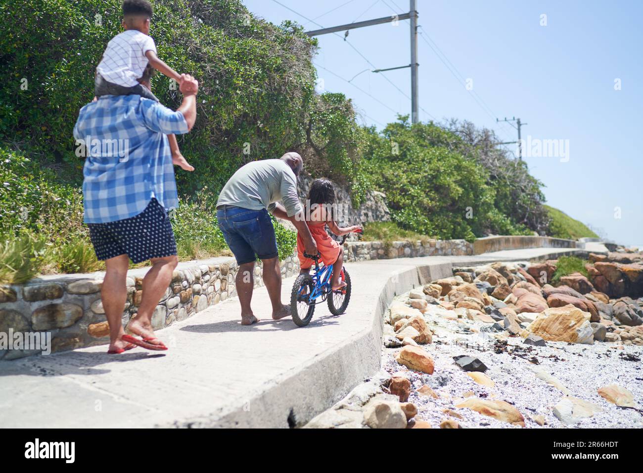 Gay male couple with kids riding bike on sunny beach boardwalk Stock Photo