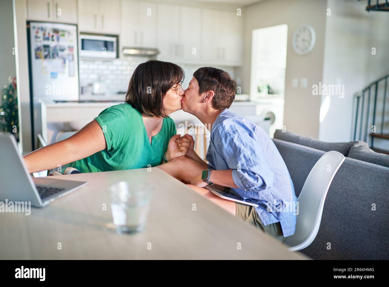 Affectionate lesbian couple kissing face to face at dining table Stock Photo