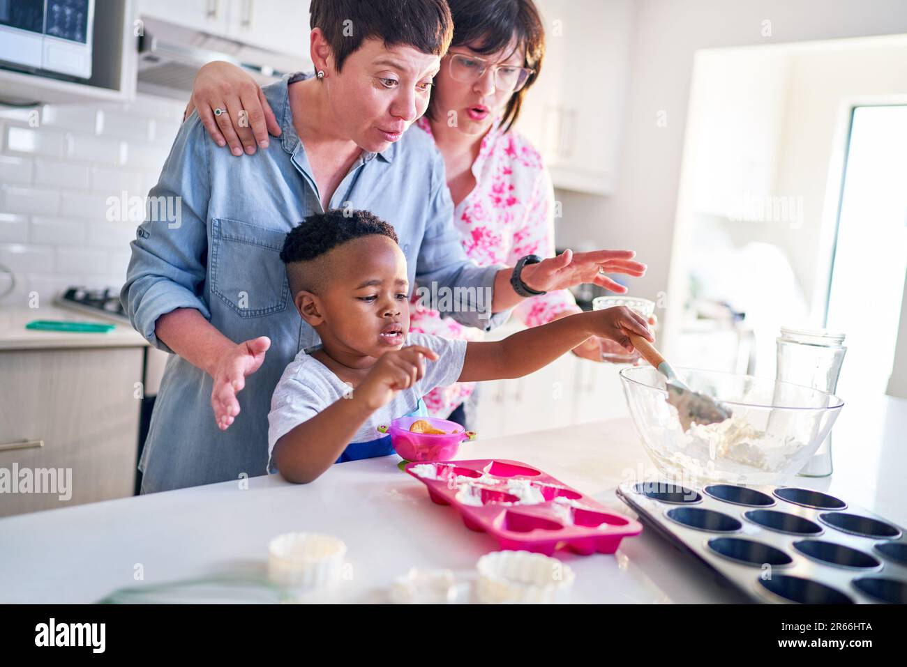 Lesbian couple and cute son baking heart-shape cupcakes in kitchen Stock Photo