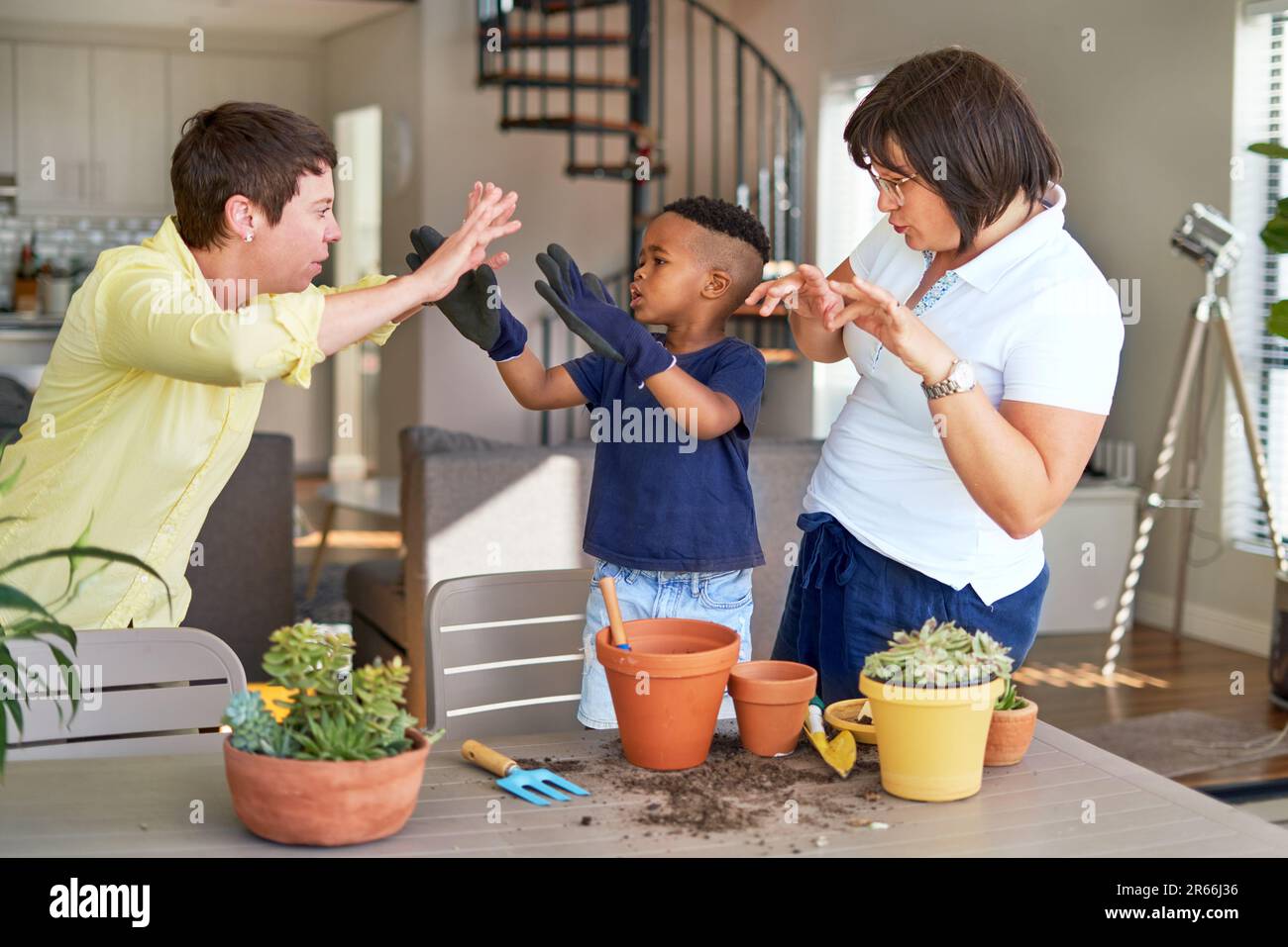 Playful lesbian couple and son gesturing, planting plants on patio Stock Photo