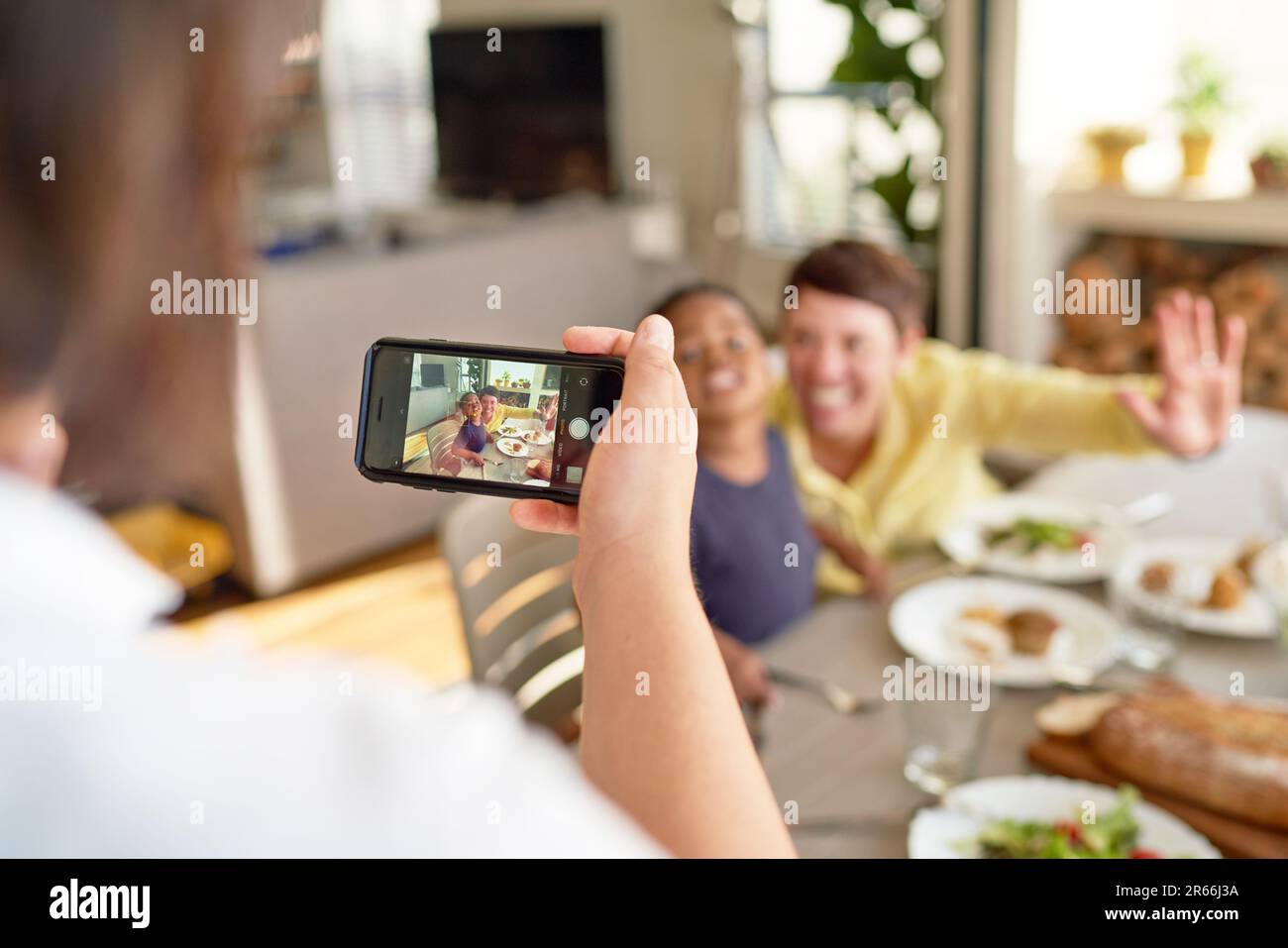 Woman with camera phone photographing wife and son at dinner table Stock Photo