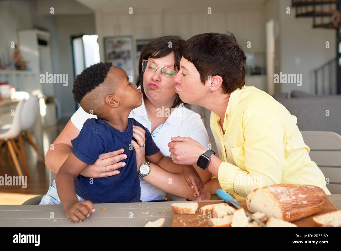 Lesbian couple and cute son puckering lips at dinner table Stock Photo