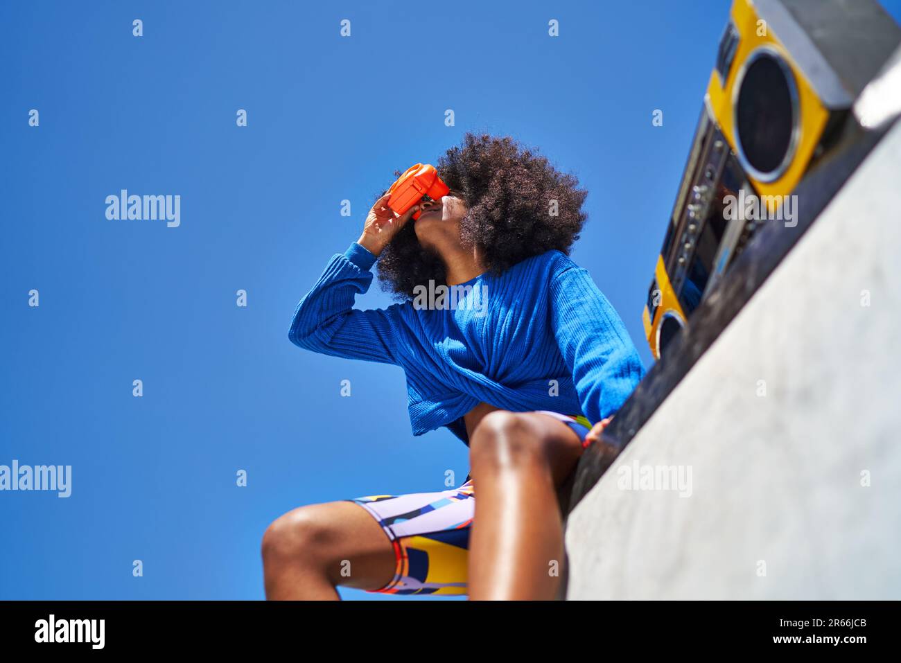 Young woman with boom box and view finder against blue sky Stock Photo