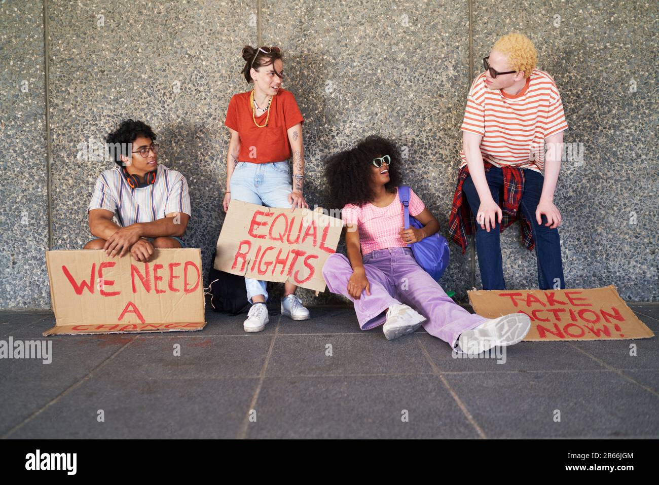 Young friends with equal rights signs resting at wall Stock Photo
