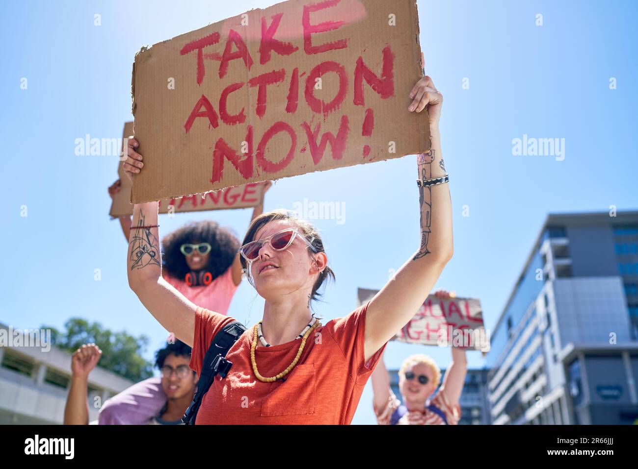 Young female protester holding action sign overhead in sunny city Stock Photo