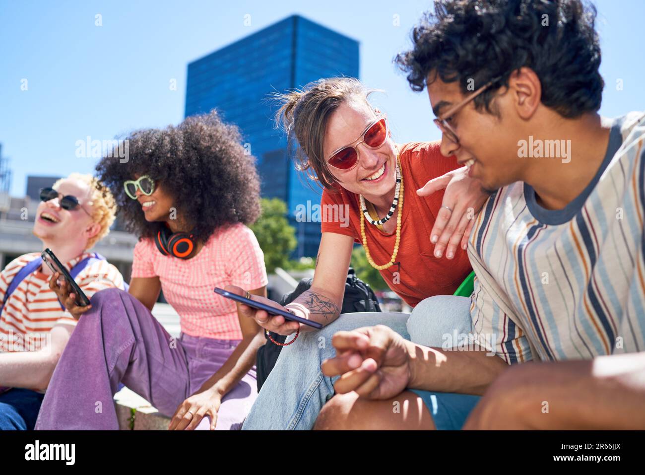 Happy young friends hanging out, using smart phone in sunny city Stock Photo