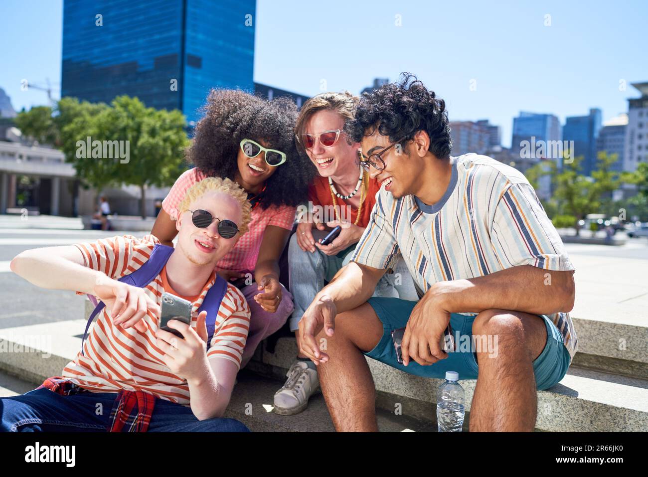 Young friends using smart phone in sunny city park Stock Photo