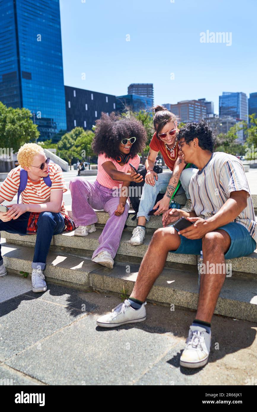 Young friends hanging out, using smart phones in sunny city park Stock Photo