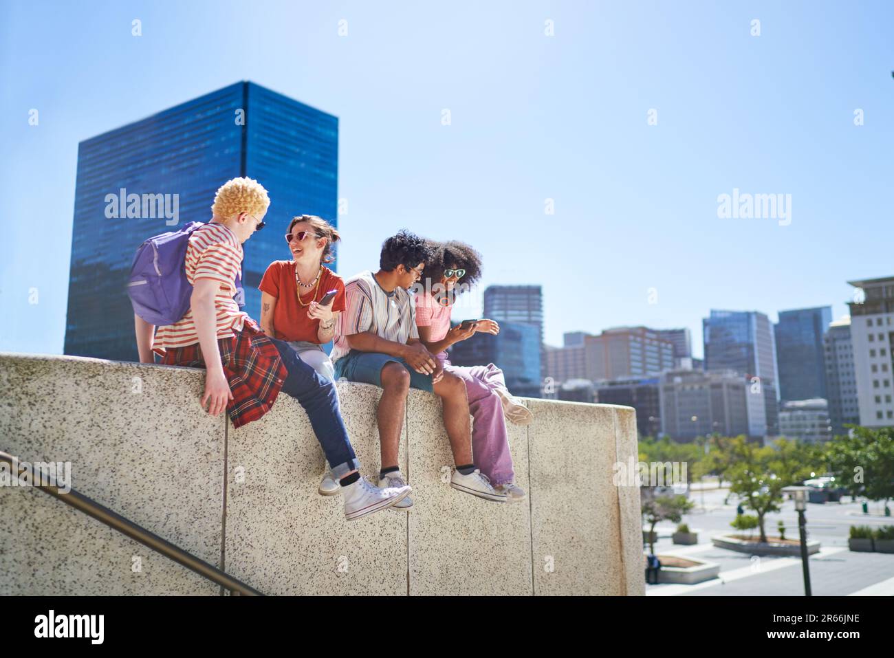 Young friends hanging out on ledge in sunny city Stock Photo
