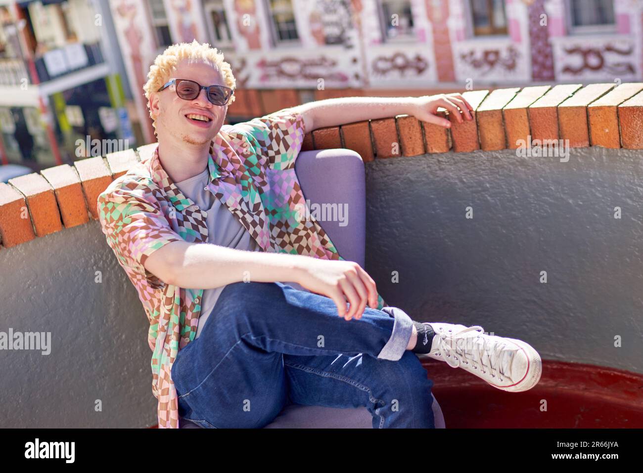 Portrait happy young albino man sitting on sunny urban rooftop Stock Photo