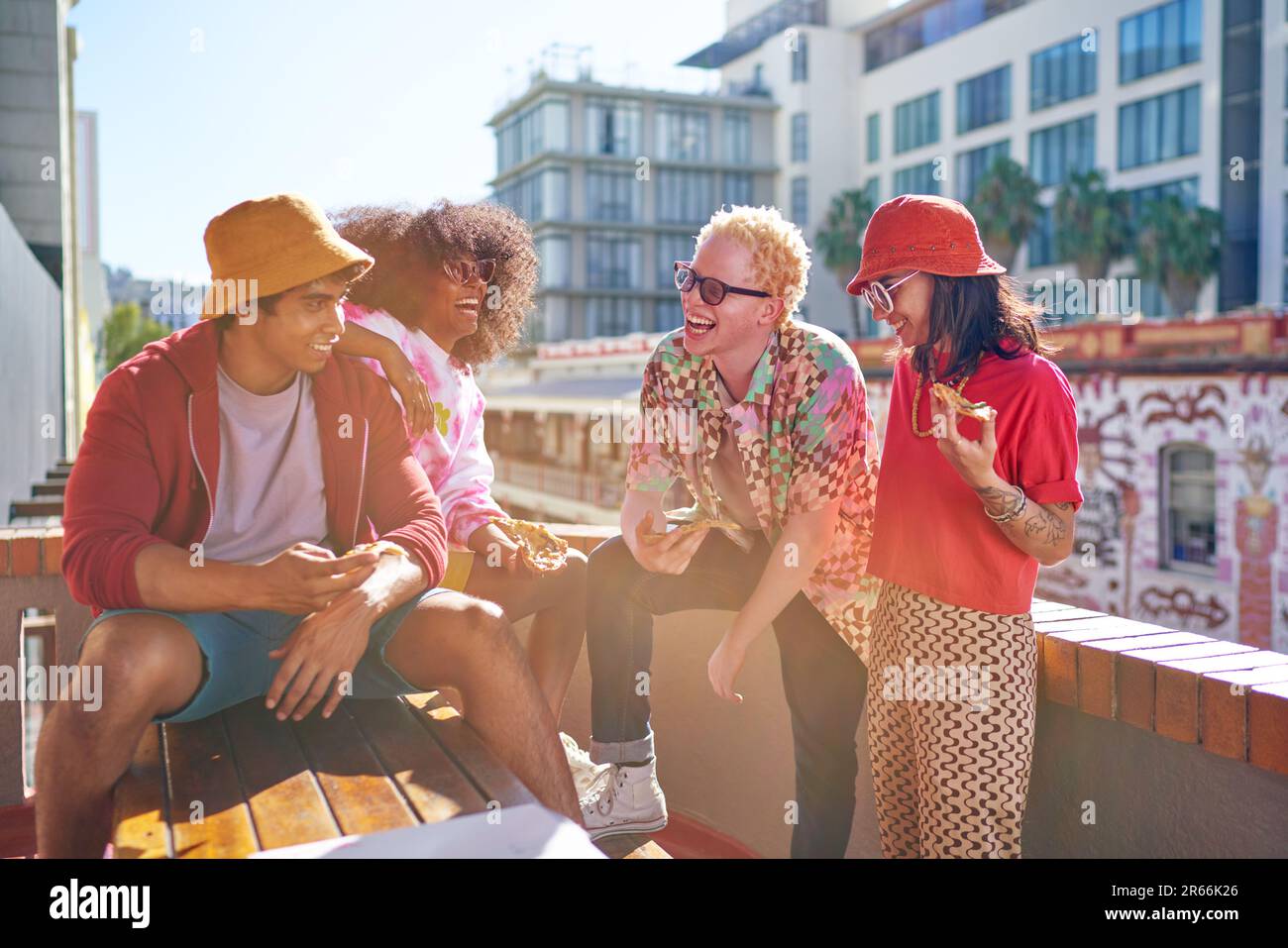 Happy young friends hanging out and eating pizza on sunny rooftop Stock Photo