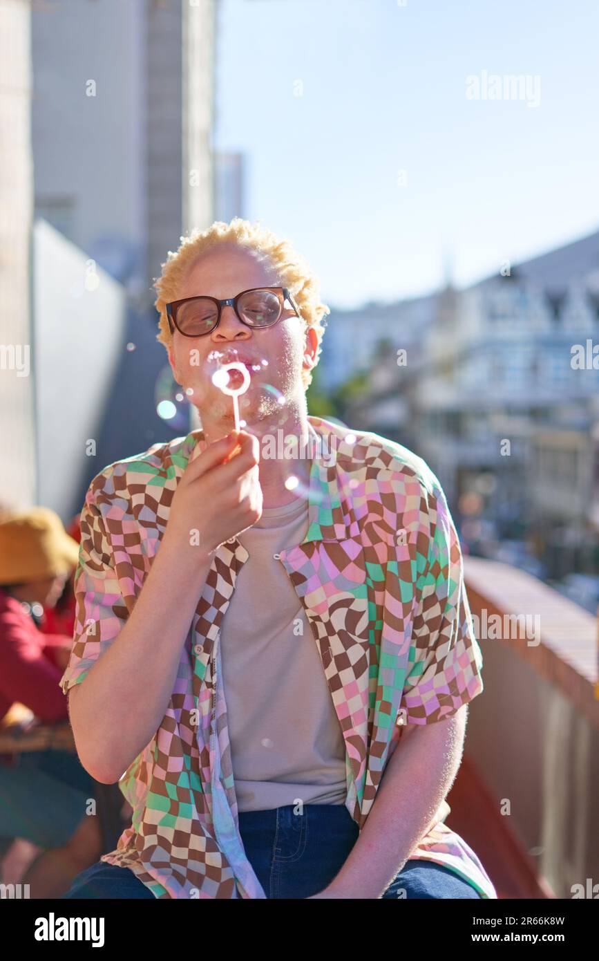 Young man blowing bubbles on sunny balcony Stock Photo