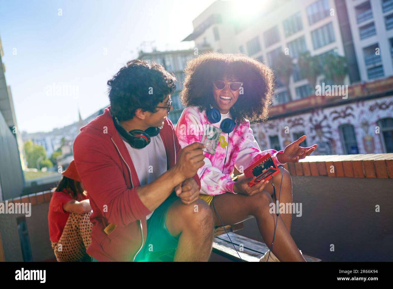 Happy young friends listening to music on sunny urban balcony Stock Photo