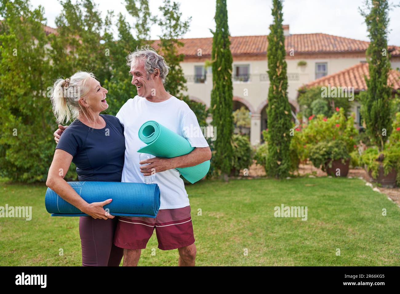 Happy senior couple with yoga mats in villa garden Stock Photo