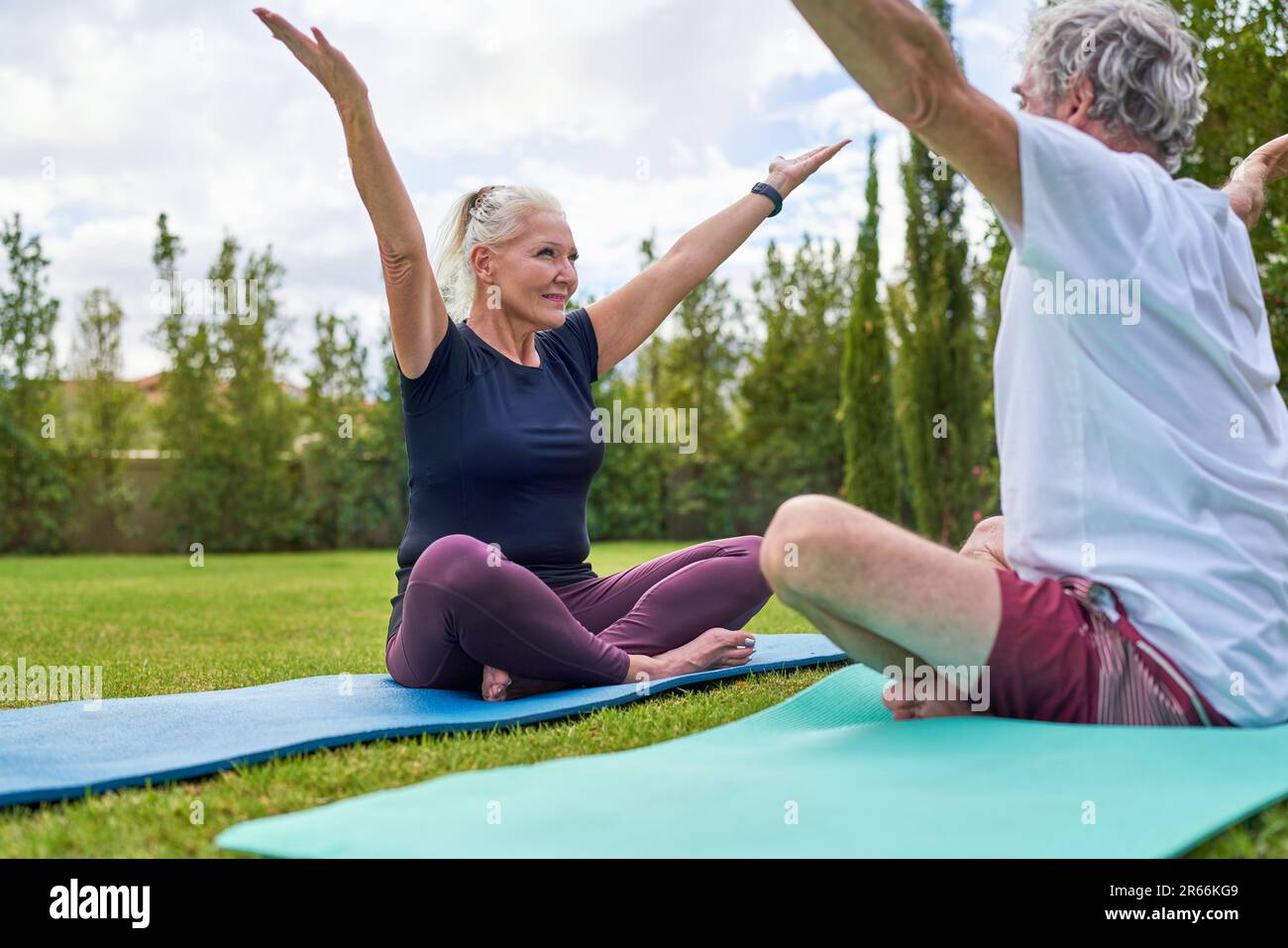 Happy senior couple practicing yoga together in park grass Stock Photo