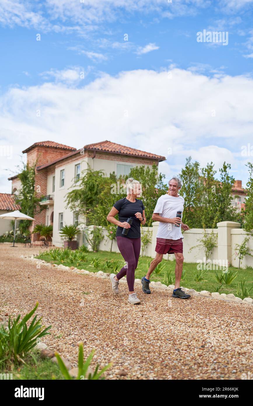 Happy senior couple jogging on footpath outside summer villa Stock Photo
