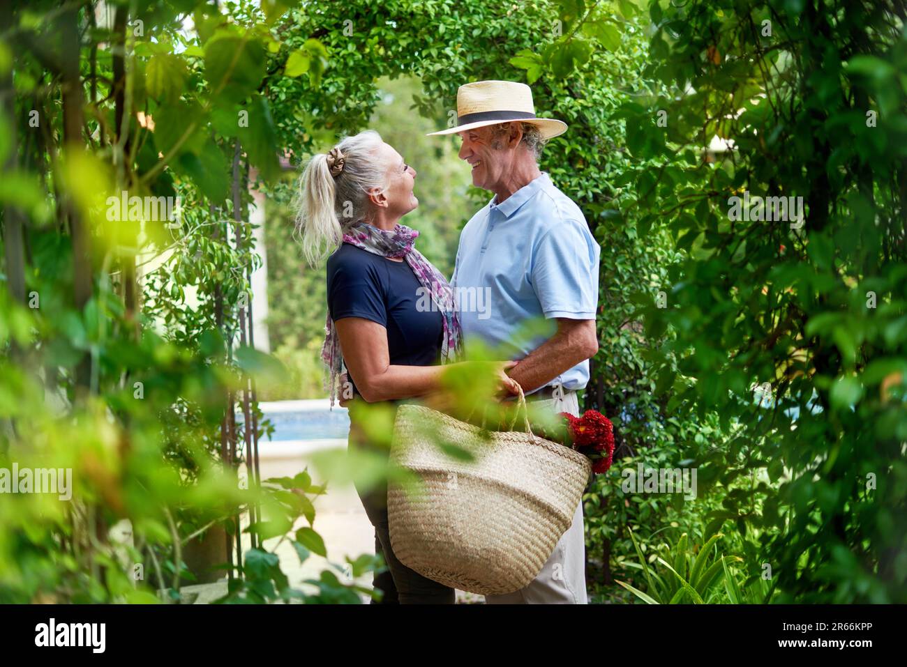 Happy senior couple hugging under lush green trellis in summer garden Stock Photo