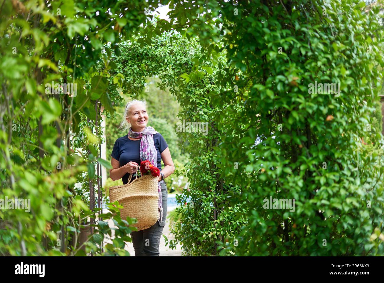 Happy senior woman walking under trellis in summer garden Stock Photo