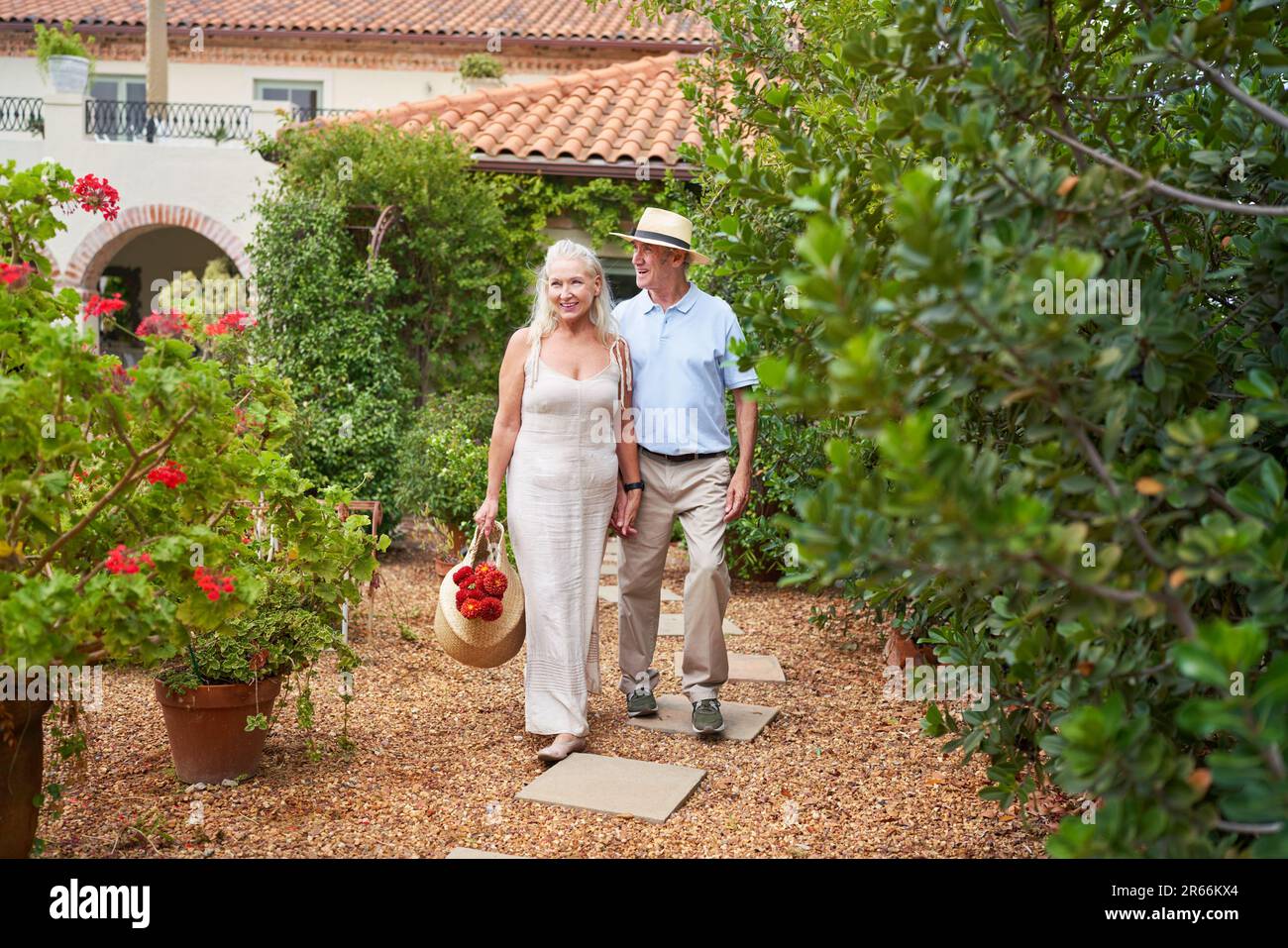 Happy senior couple with flowers walking in garden outside villa Stock Photo