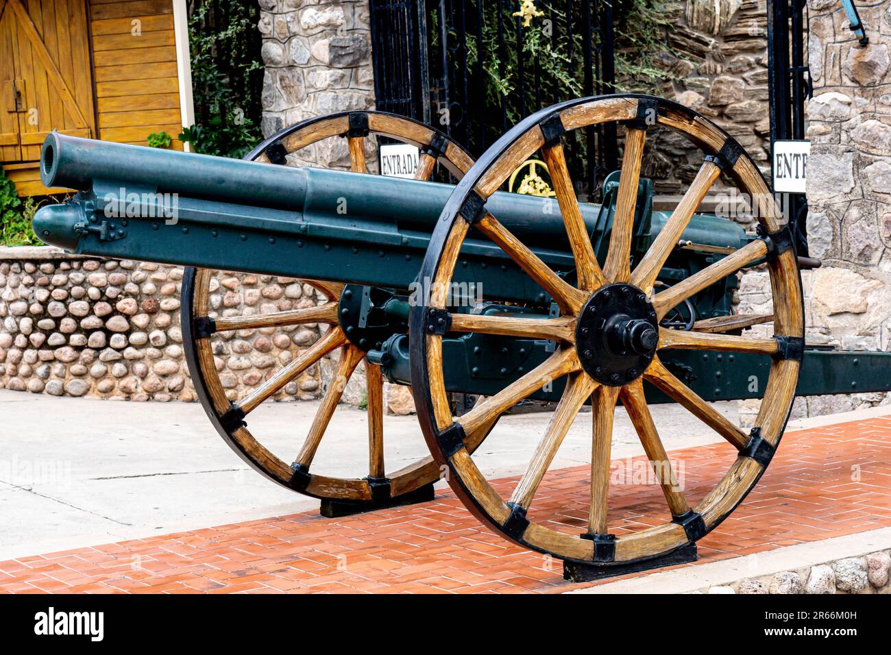 A vintage cannon is displayed prominently in a courtyard featuring red brick walls, with a cobblestone floor and a well-manicured lawn Stock Photo