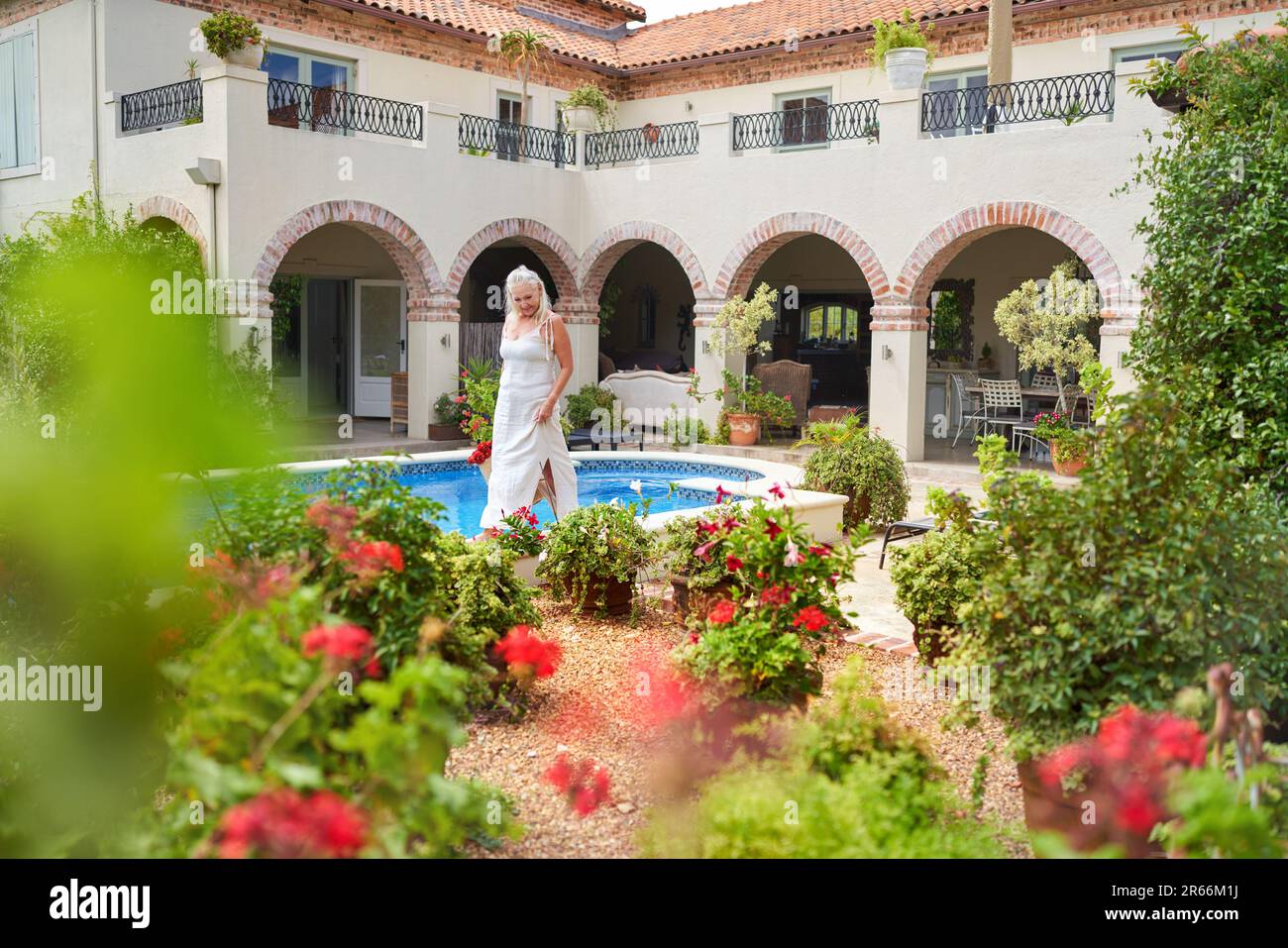 Senior woman walking along swimming pool in summer villa garden Stock Photo