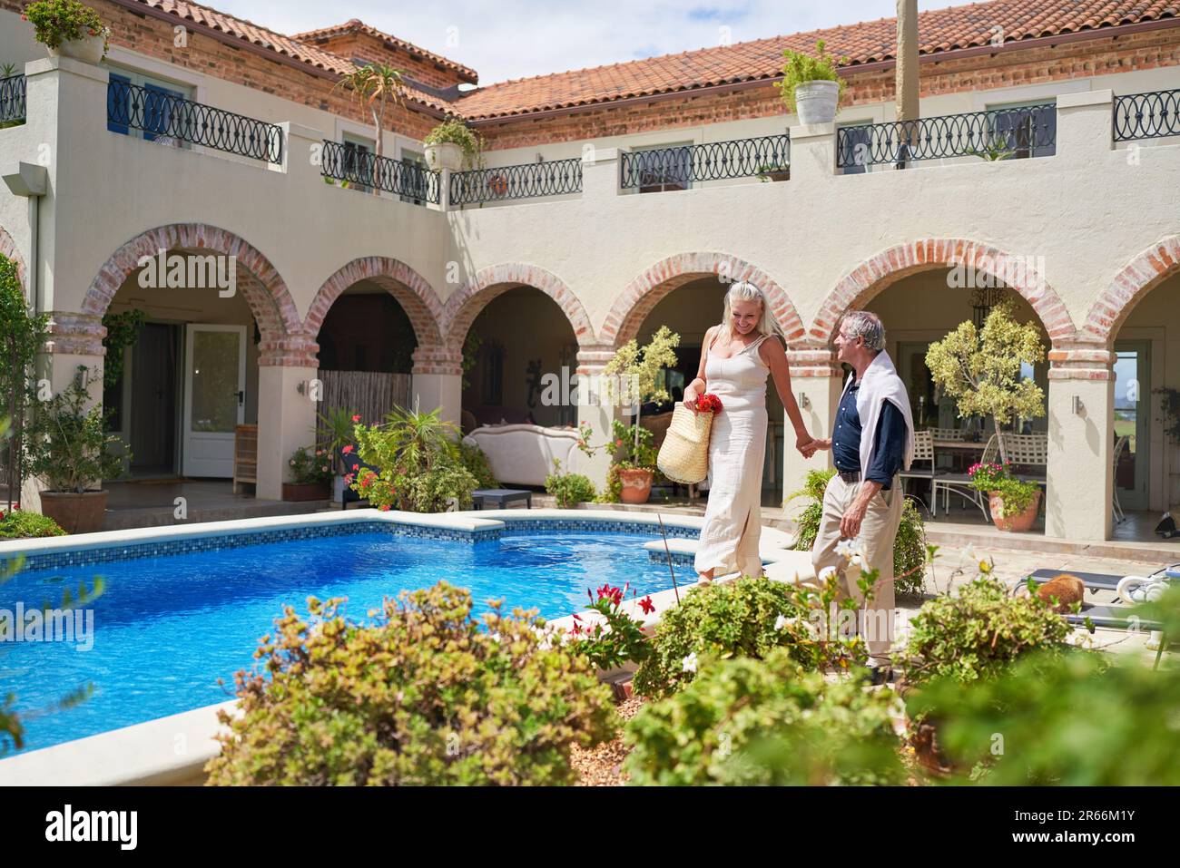 Happy senior couple walking along swimming pool on sunny villa patio Stock Photo