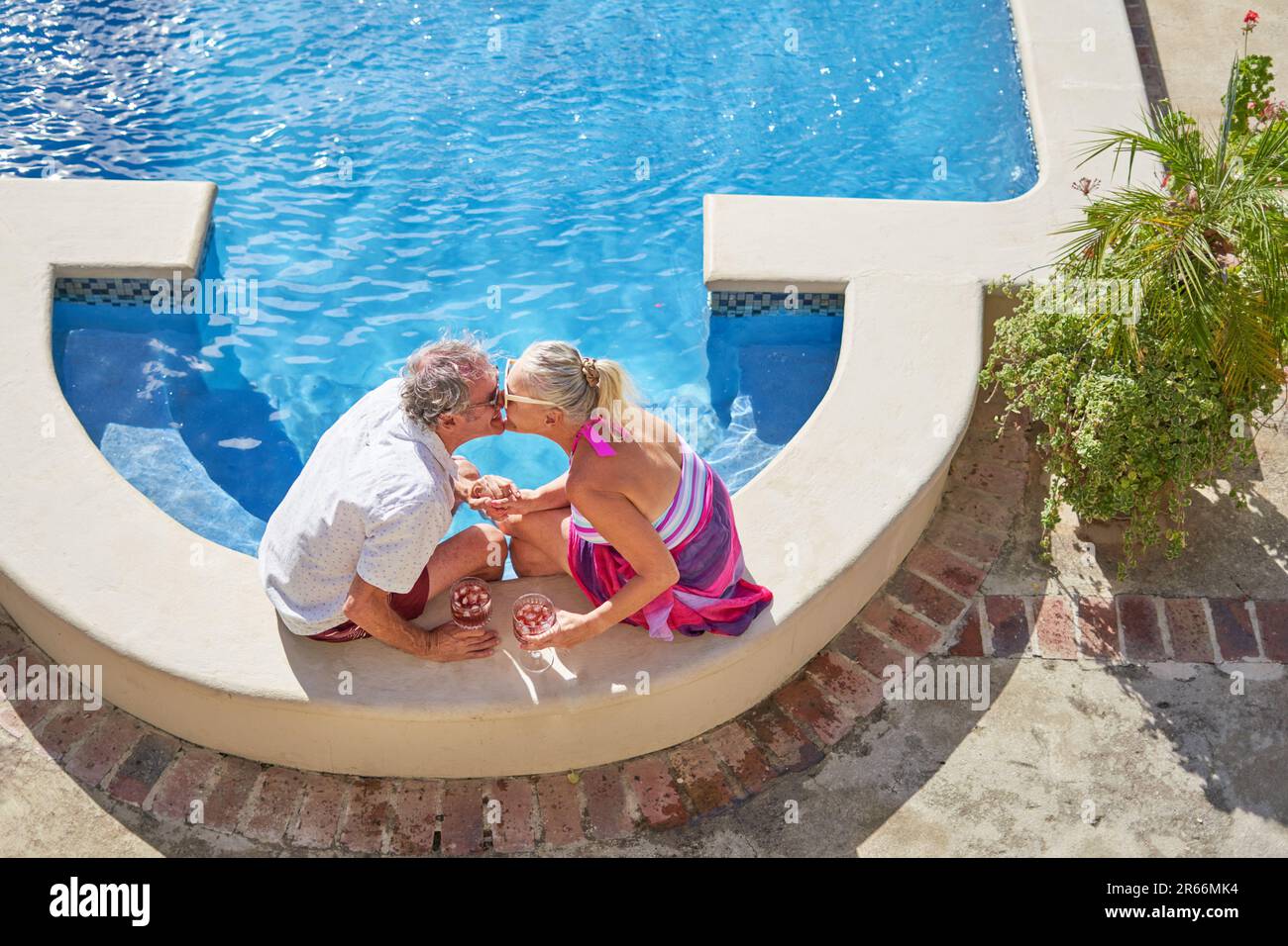 Affectionate senior couple kissing at sunny summer swimming pool Stock Photo