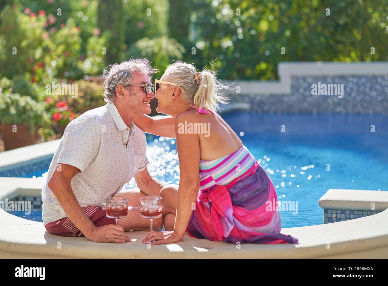 Happy, affectionate senior couple kissing and drinking at swimming pool Stock Photo