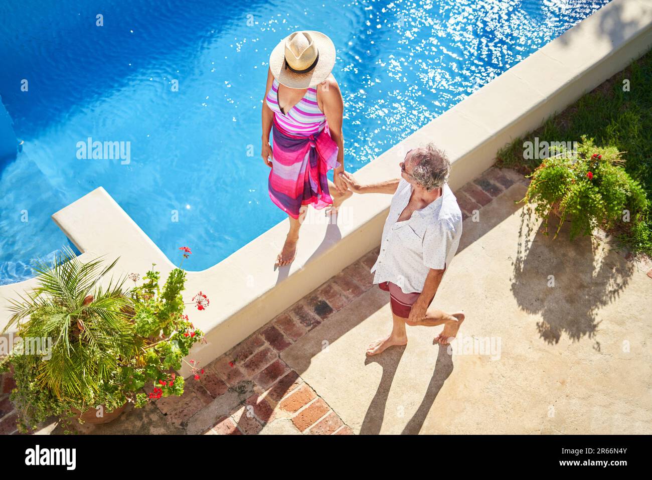 Senior couple holding hands, walking along summer swimming pool Stock Photo