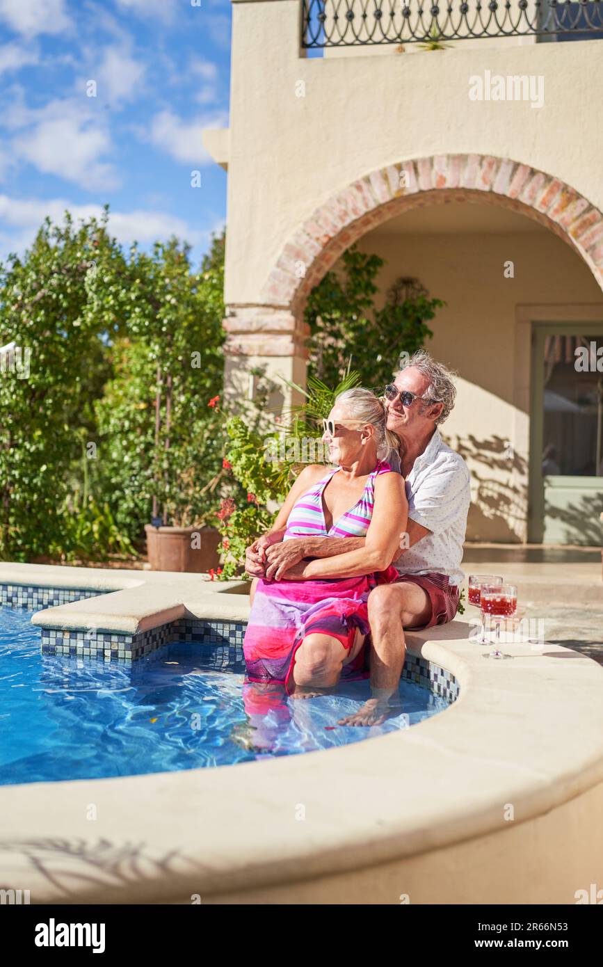 Carefree senior couple relaxing at swimming pool on villa patio Stock Photo