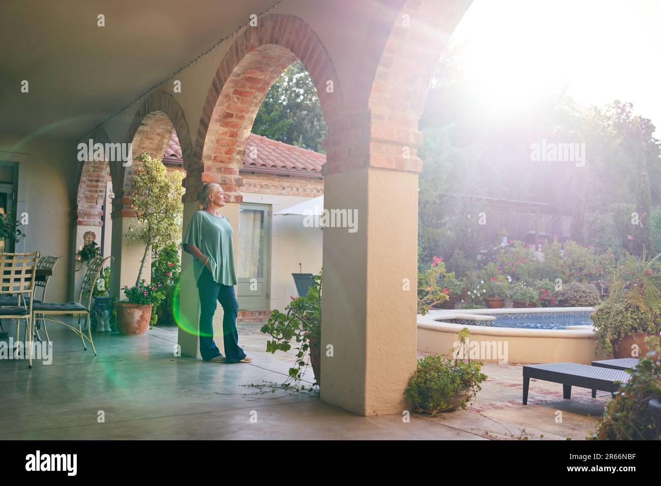 Serene, thoughtful senior woman standing on sunny villa patio Stock Photo