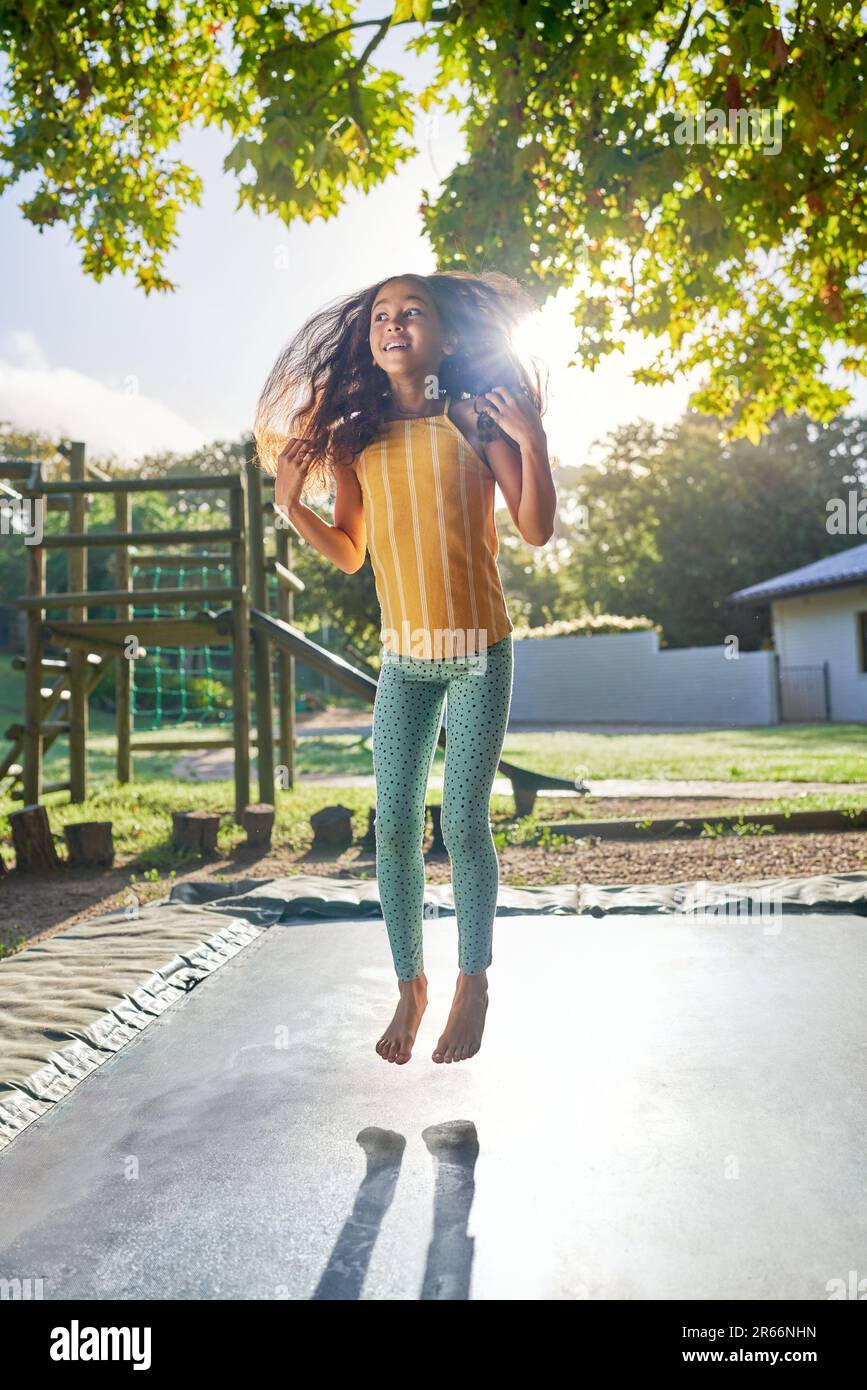 Carefree, barefoot girl jumping on trampoline in sunny backyard Stock Photo