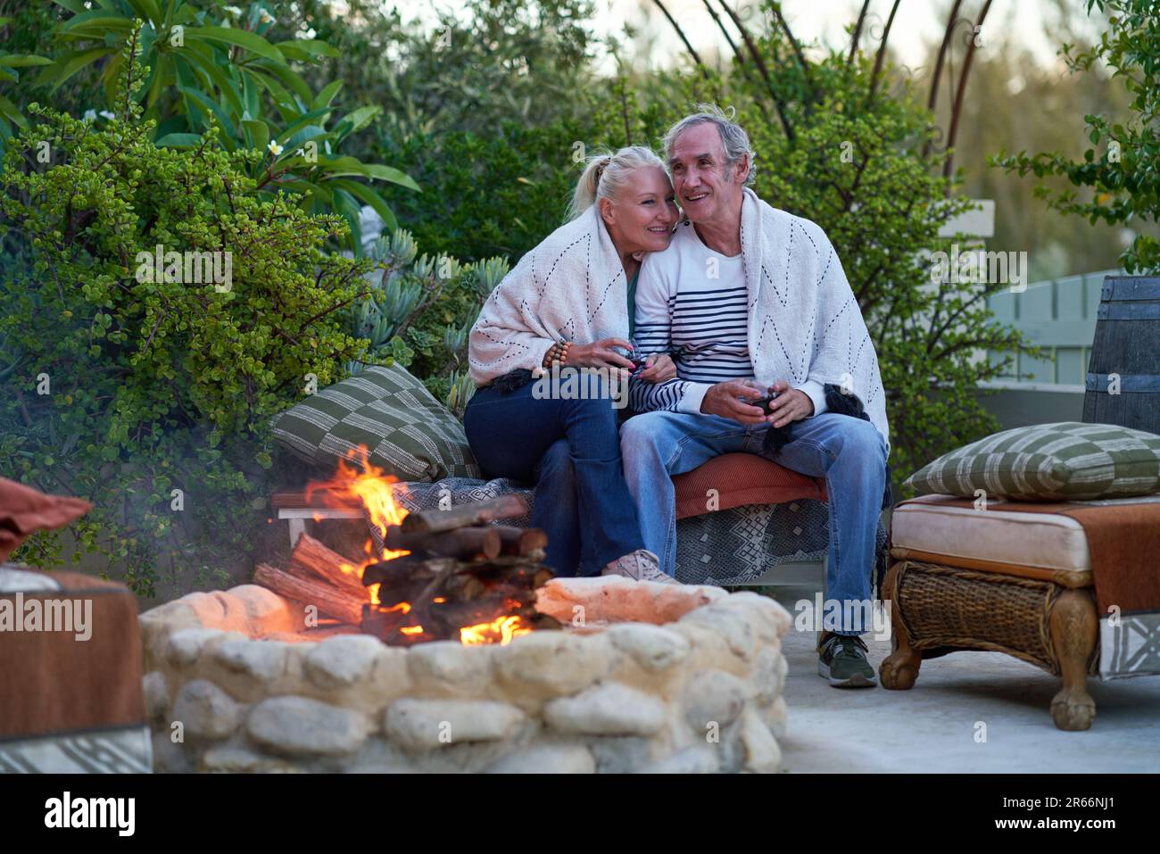 Happy senior couple sitting and drinking wine at fire pit on patio Stock Photo
