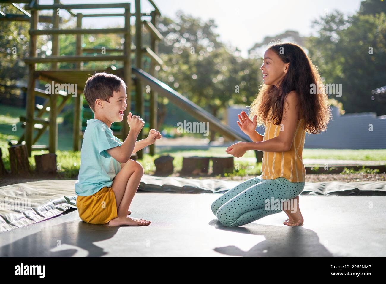 Happy brother and sister playing clapping game on sunny trampoline Stock Photo