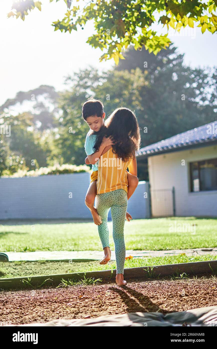 Sister carrying cute brother in sunny summer backyard Stock Photo