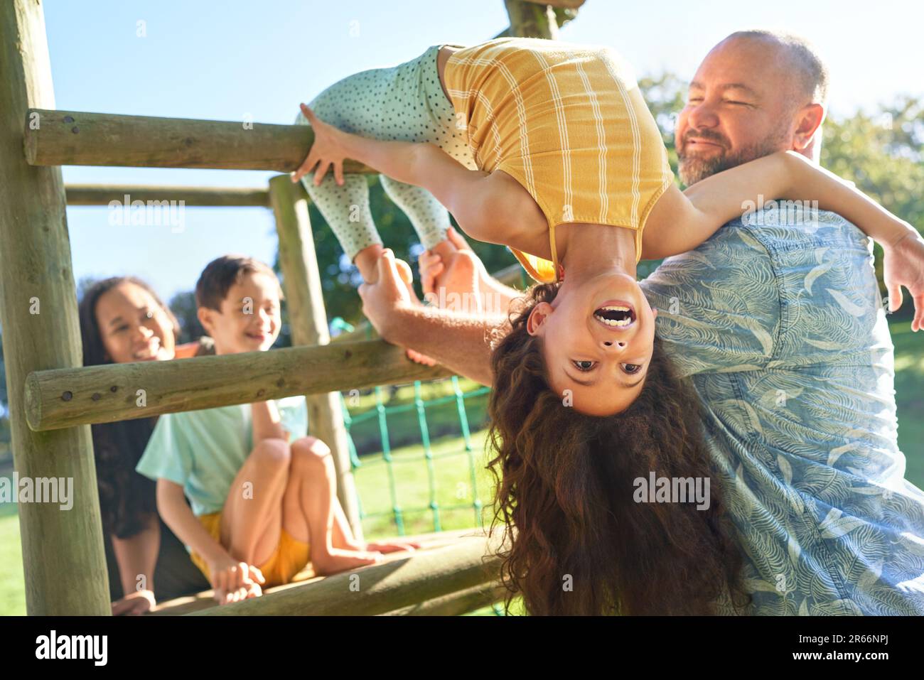 Father holding daughter upside-down, playing in sunny backyard Stock Photo