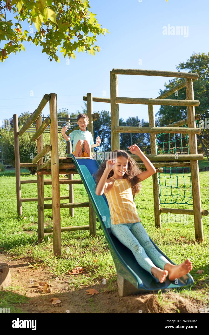 Carefree brother and sister playing on slide at playground structure Stock Photo