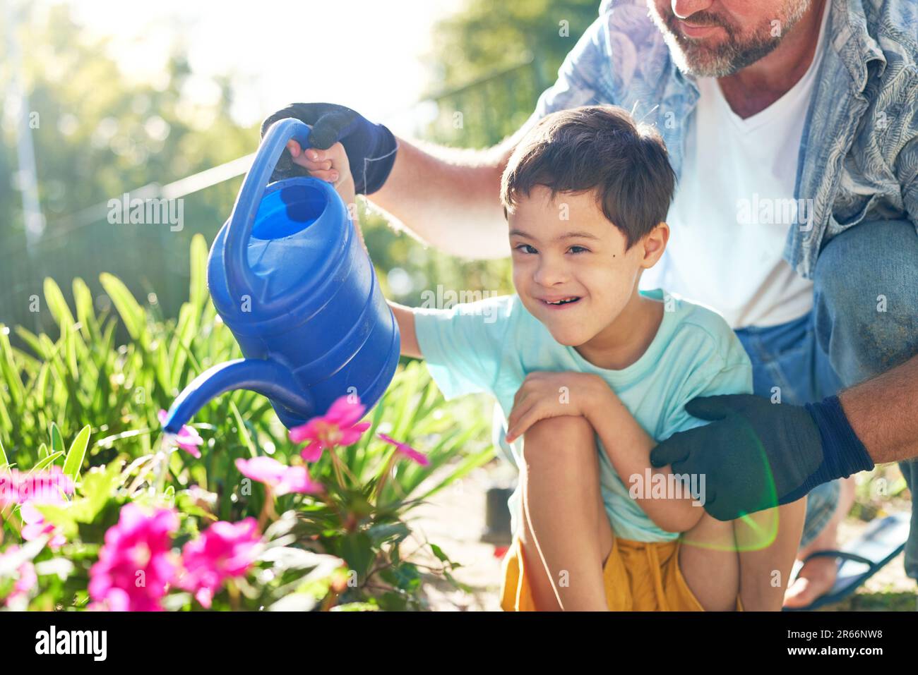 Portrait happy boy with Down Syndrome watering flowers with father Stock Photo