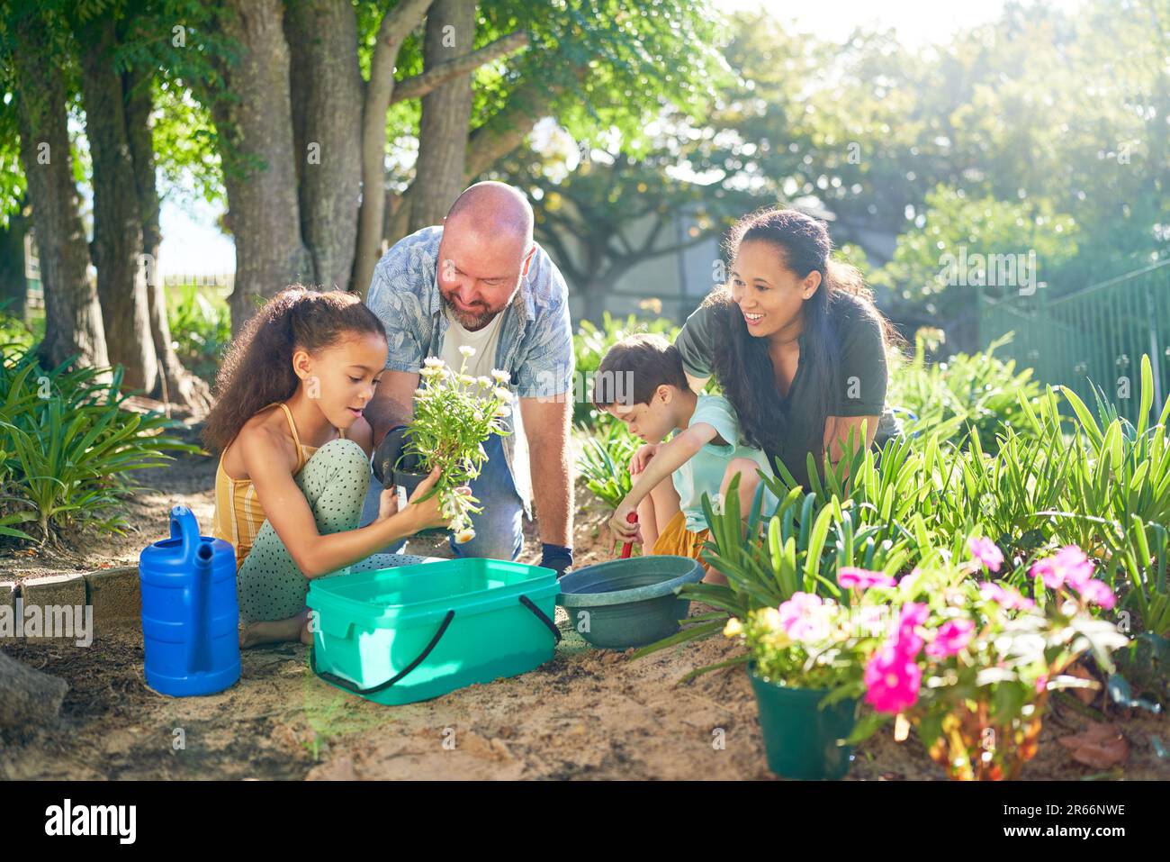 Happy family planting flowers in sunny summer garden Stock Photo