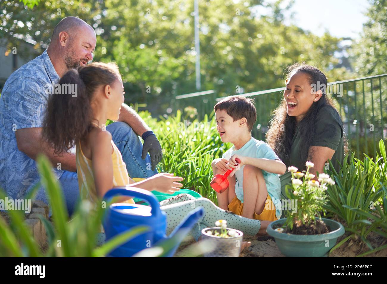 Happy family laughing, planting flowers in summer garden Stock Photo