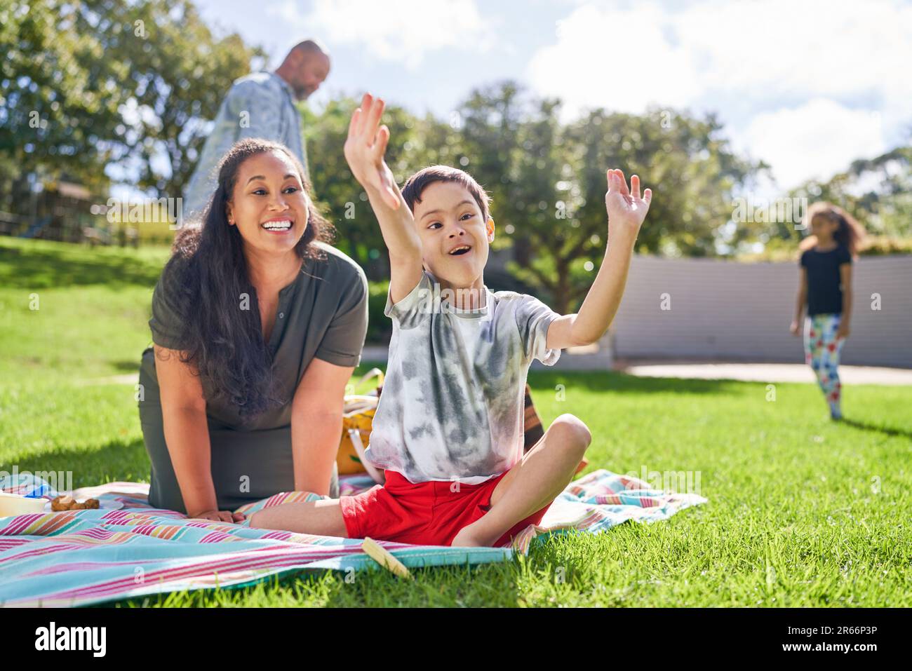 Happy mother watching cute son with Down Syndrome eating in park Stock Photo