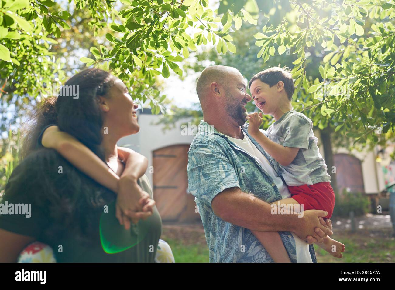 Happy parents and son with Down Syndrome below sunny tree Stock Photo