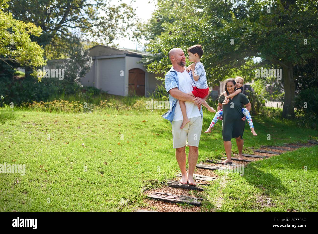 Happy parents carrying daughter and son on path in sunny backyard Stock Photo