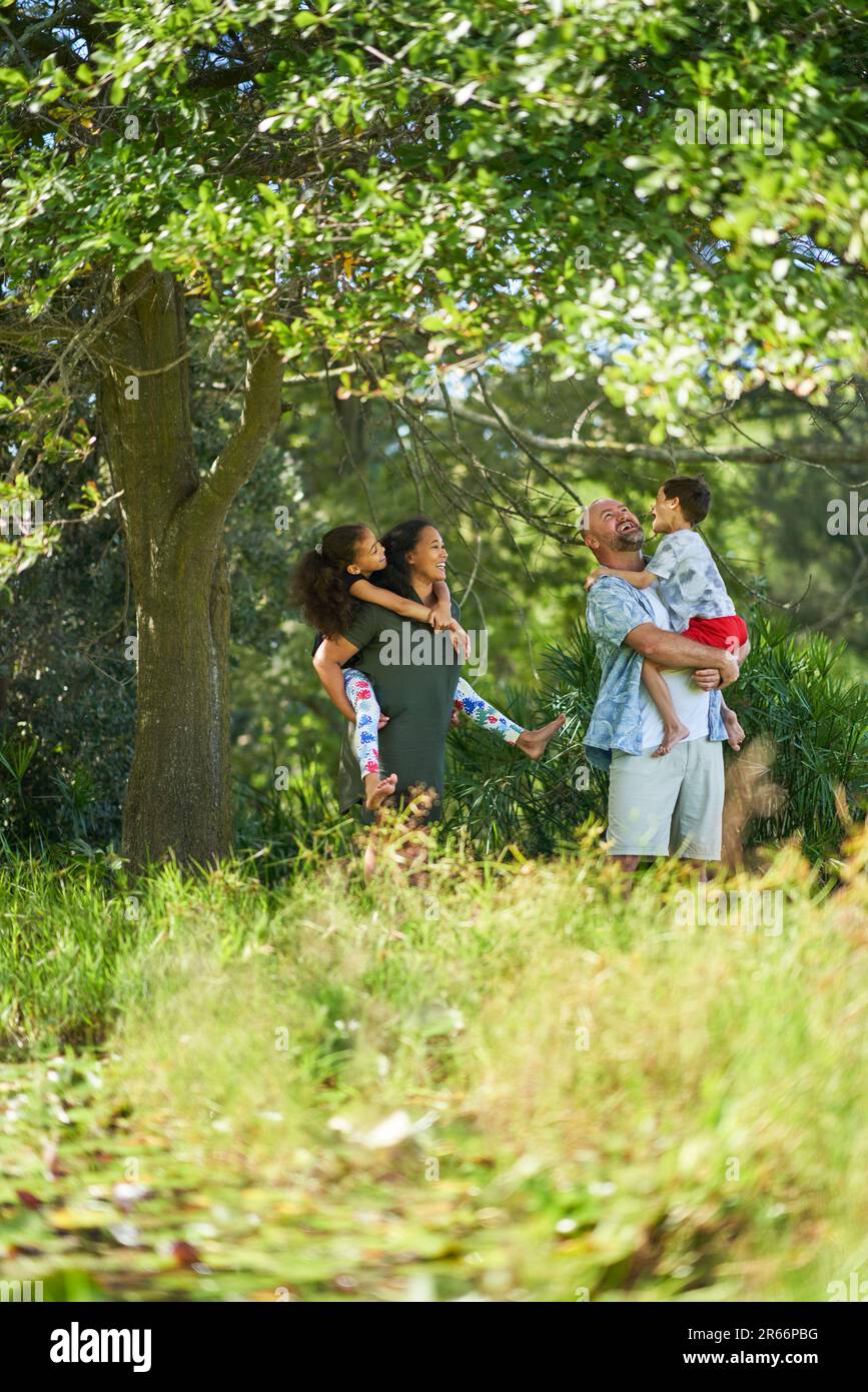 Happy family standing below tree in sunny summer park Stock Photo