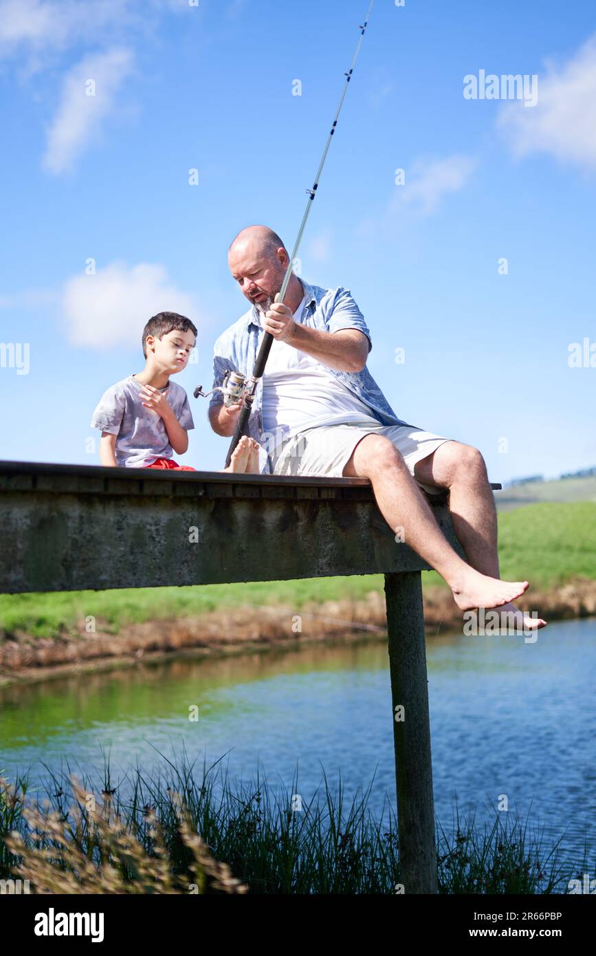 Father teaching son with Down Syndrome fishing on summer dock Stock Photo